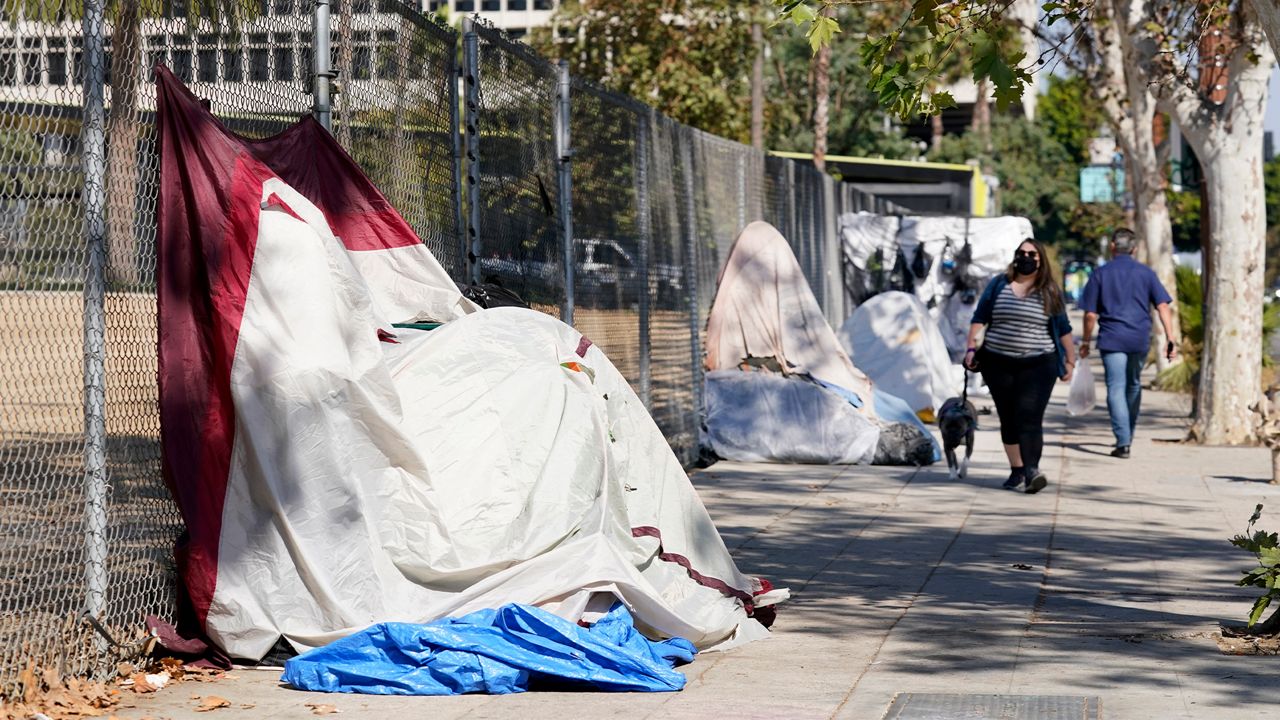 Pedestrians walk past a homeless encampment just outside Grand Park, Wednesday, Oct. 28, 2020, in Los Angeles. (AP Photo/Chris Pizzello)