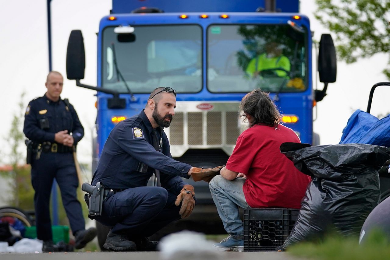 Police officer Michael Bennis speaks to a man at a homeless camp that was being cleared by city workers, Tuesday, May 16, 2023, in Portland, Maine.  Maine's largest city started removing a large encampment as it grapples with homelessness and packed shelters.  (AP Photo/Robert F. Bukaty)