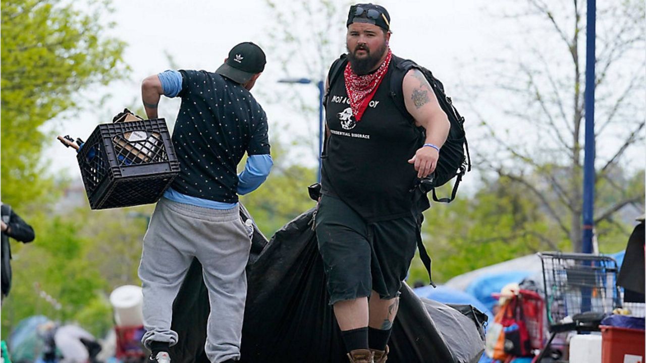 A man helps an inhabitant of a homeless encampment move belongings before city workers arrived to clean up the area, Tuesday, May 16, 2023, in Portland, Maine.  Maine's largest city started removing a large encampment as it grapples with homelessness and packed shelters. (AP Photo/Robert F. Bukaty)