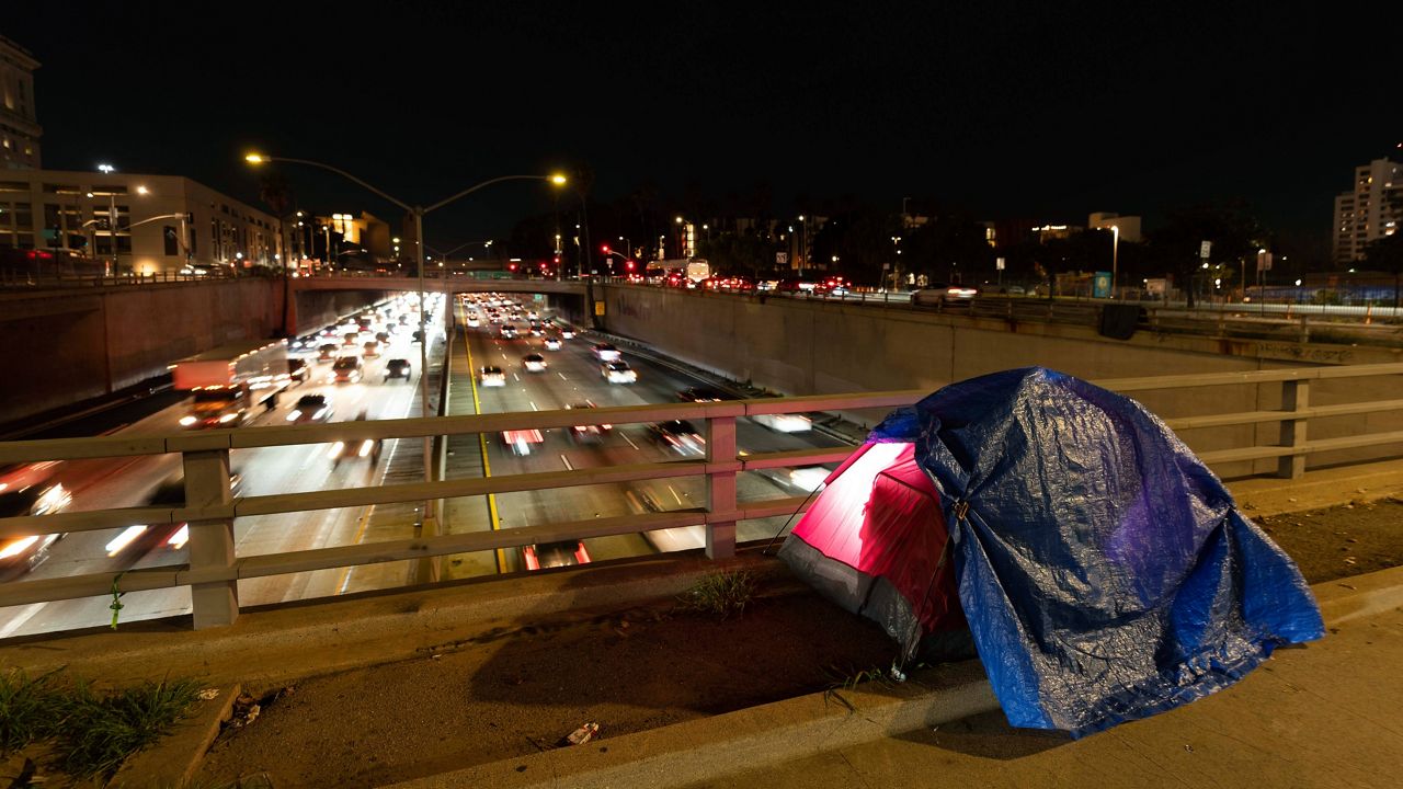 In this photo illuminated by an off-camera flash, a tarp covers a portion of a homeless person's tent on a bridge overlooking the 101 Freeway in Los Angeles, Thursday, Feb. 2, 2023. (AP Photo/Jae C. Hong, File)