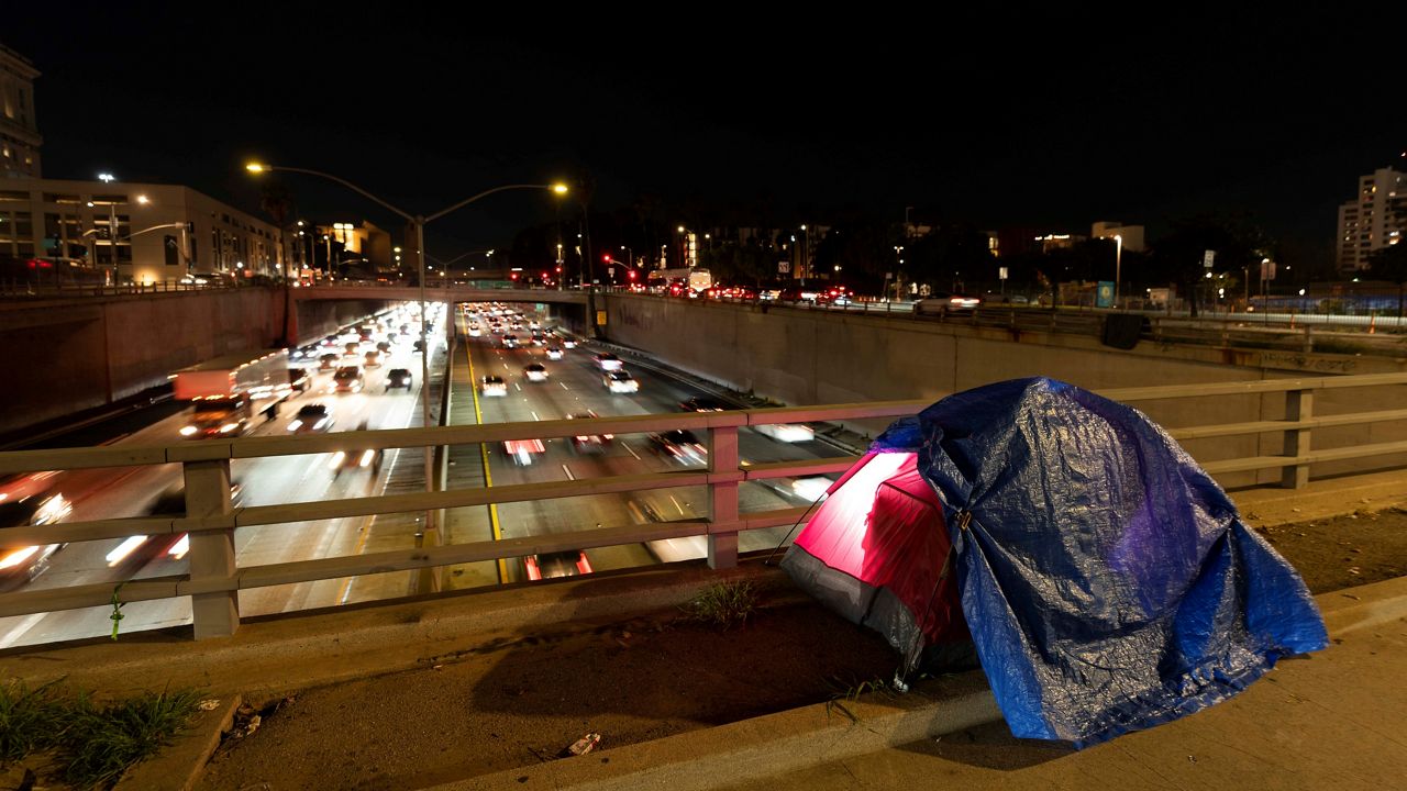 In this photo illuminated by an off-camera flash, a tarp covers a portion of a homeless person's tent on a bridge overlooking the 101 Freeway in Los Angeles, Thursday, Feb. 2, 2023. (AP Photo/Jae C. Hong, File)
