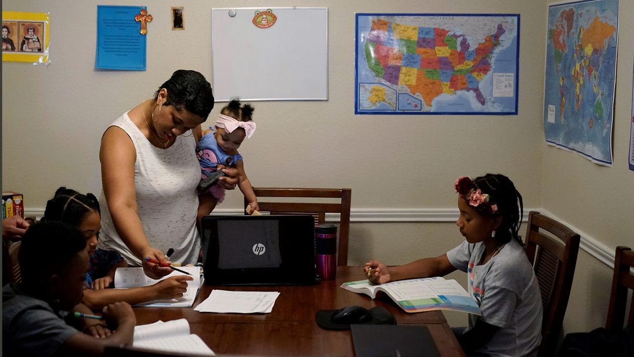 Arlena Brown holds her youngest child as she leads her other three children through math practice at their home in Austin. (AP Photo/Eric Gay)