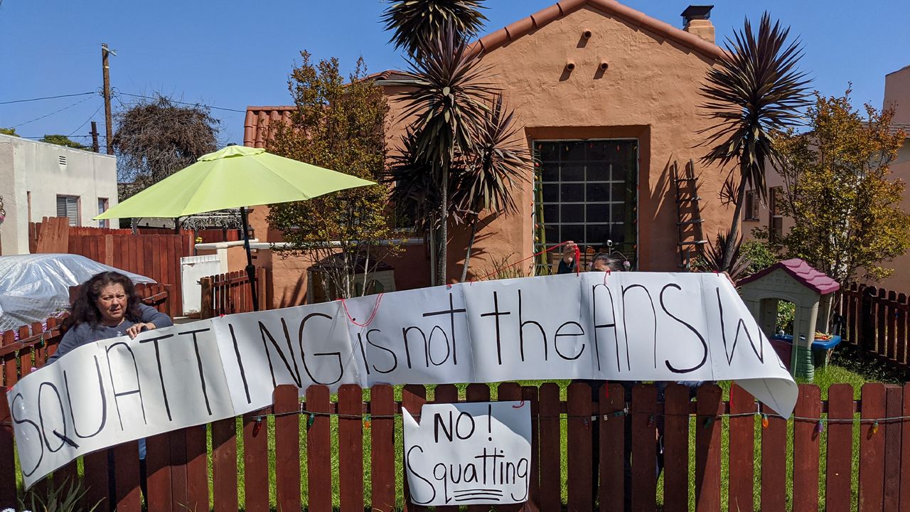 Resident Marie Salas, left, sets a banner on her home fence reading" Squatting is not the Answer," across the street of a formerly vacant home that was recently taken by a group of homeless mothers in El Sereno neighborhood of Los Angeles Monday, March 30, 2020. (AP Photo/Damian Dovarganes)