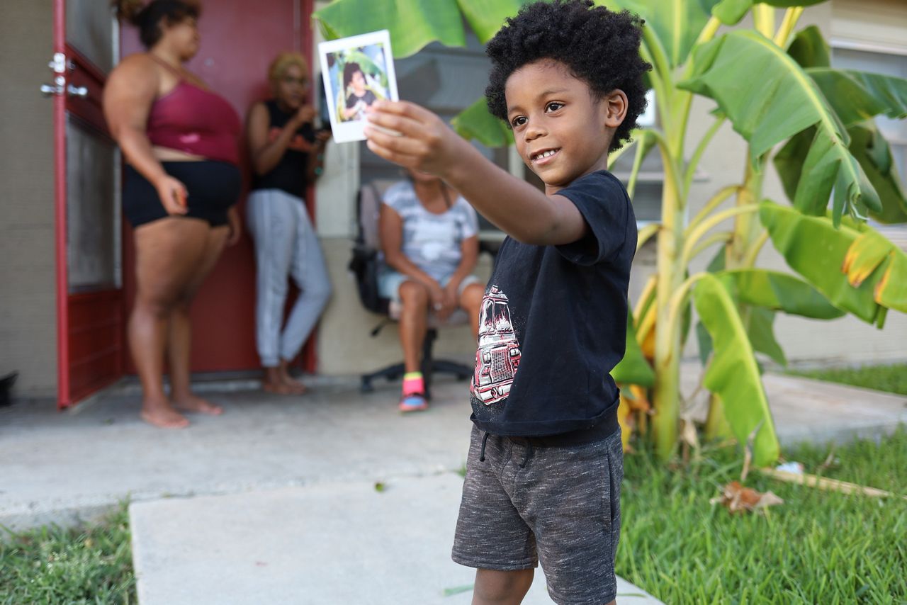 A child named Hakeem holds up a photo Francisco Cortés took of him in the Cassiano Homes. (Spectrum News 1/Jose Arredondo)