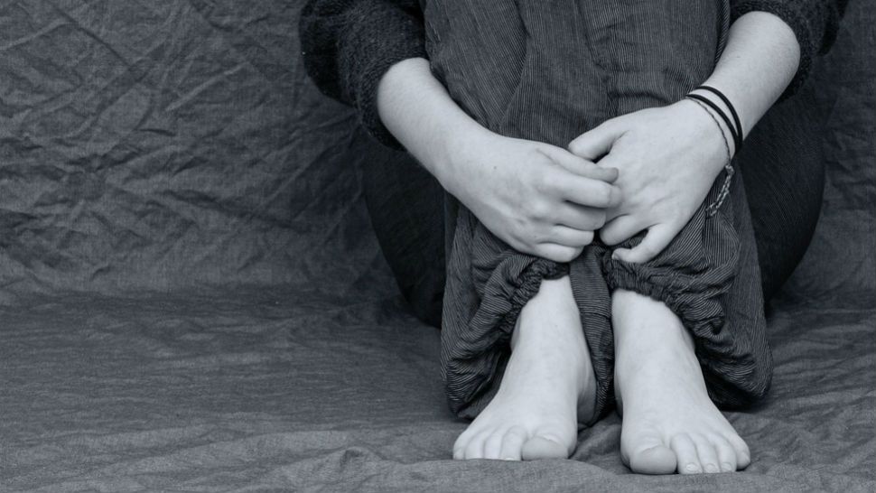 Black and white file photo of a person sitting and hugging their legs. 