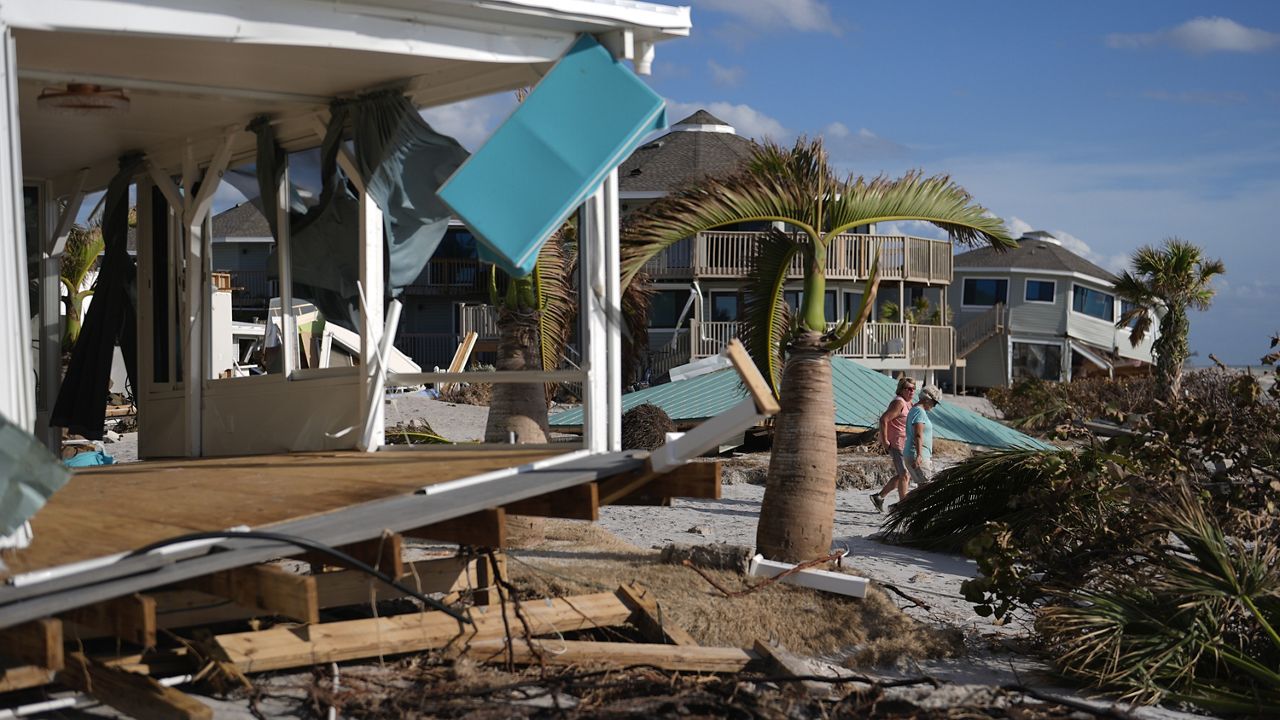 Resident Kerry Flynn, right, and a friend walk past a damaged home and the displaced roof of their 55+ mobile home community's tiki hut after the passage of Hurricane Milton, on Manasota Key, in Englewood, Fla., Oct. 13, 2024. (AP Photo/Rebecca Blackwell)