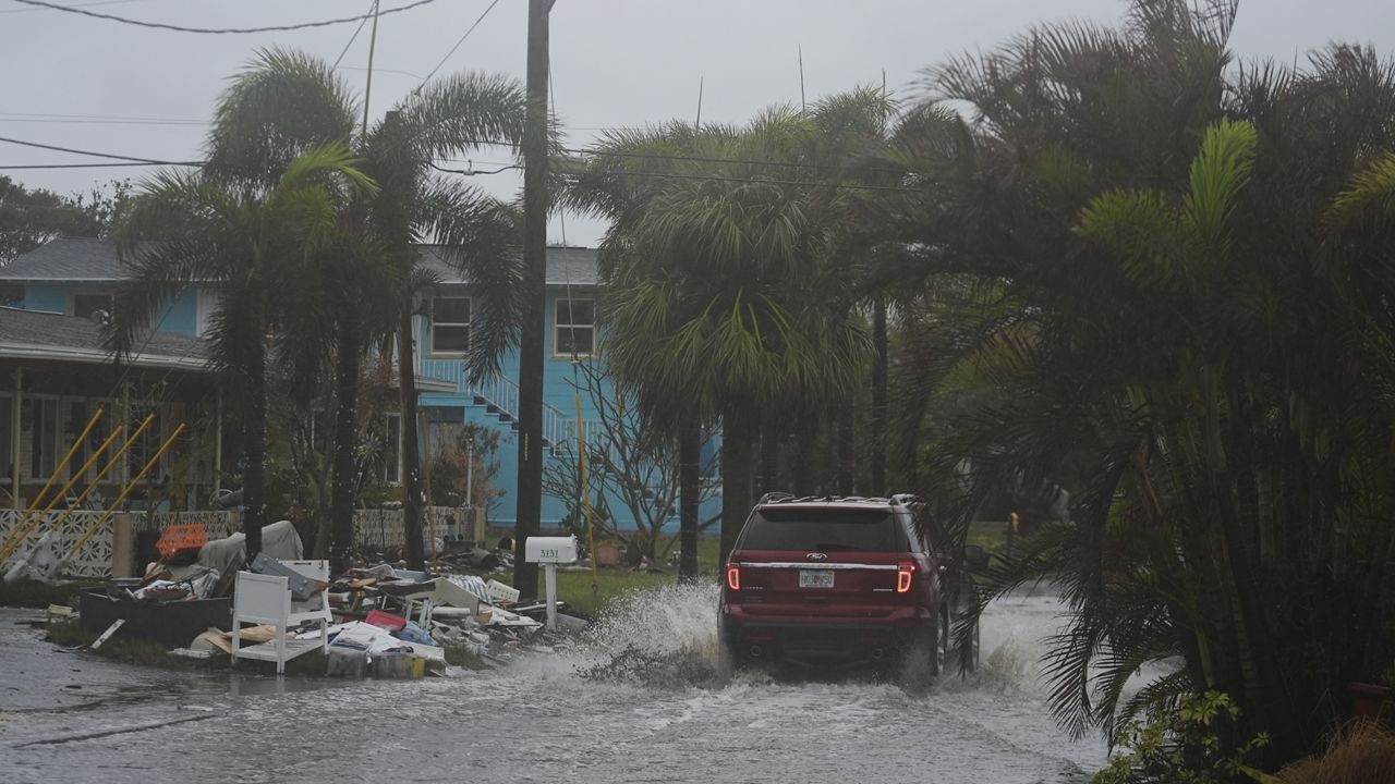 A car drives past a pile of debris from Hurricane Helene flooding, along a street that had already begun flooding from rain ahead of the arrival of Hurricane Milton, in Gulfport, Fla., Wednesday, Oct. 9, 2024. (AP Photo/Rebecca Blackwell)