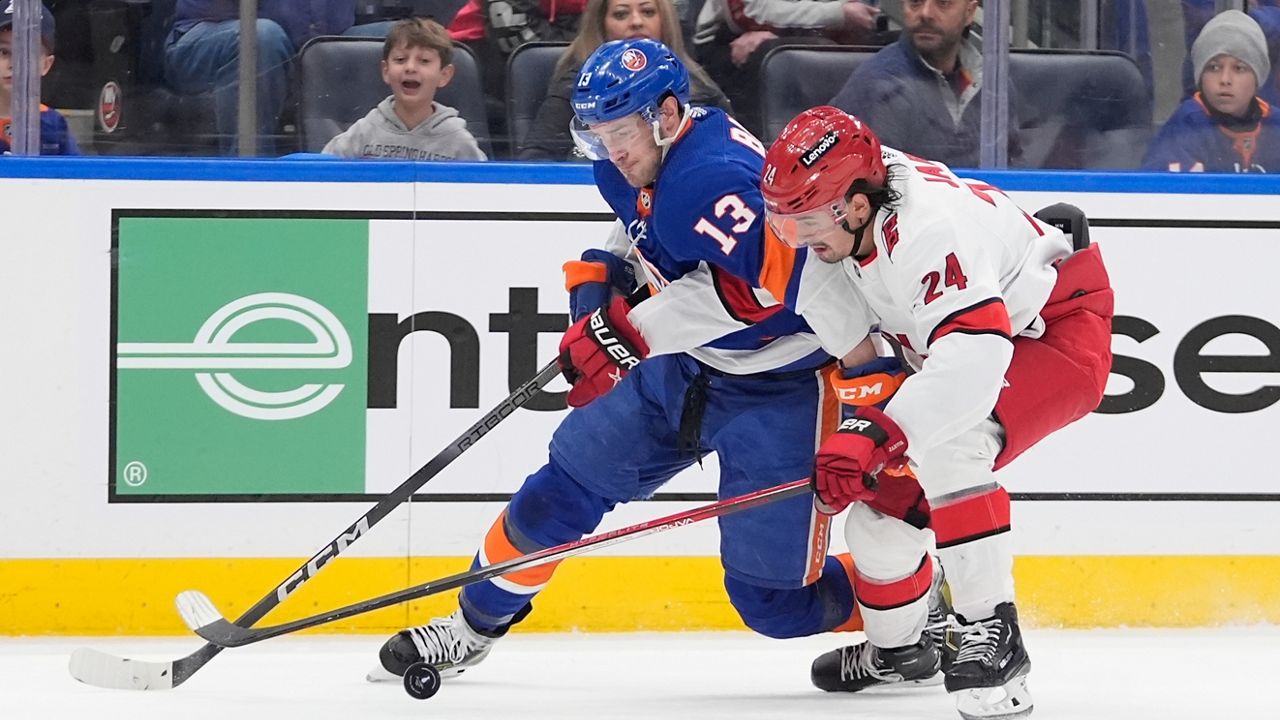 Carolina Hurricanes' Seth Jarvis (24) fights for control of the puck with New York Islanders' Mathew Barzal (13) during the first overtime period of Game 4 of an NHL hockey Stanley Cup first-round playoff series Saturday, April 27, 2024, in Elmont, N.Y. (AP Photo/Frank Franklin II)