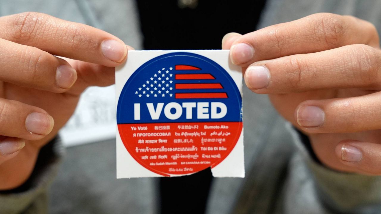 An election volunteer offers voters an "I Voted" sticker after casting their ballot on Super Tuesday, at the Ranchito Elementary School polling station in the Panorama City section of Los Angeles. (AP Photo/Richard Vogel)