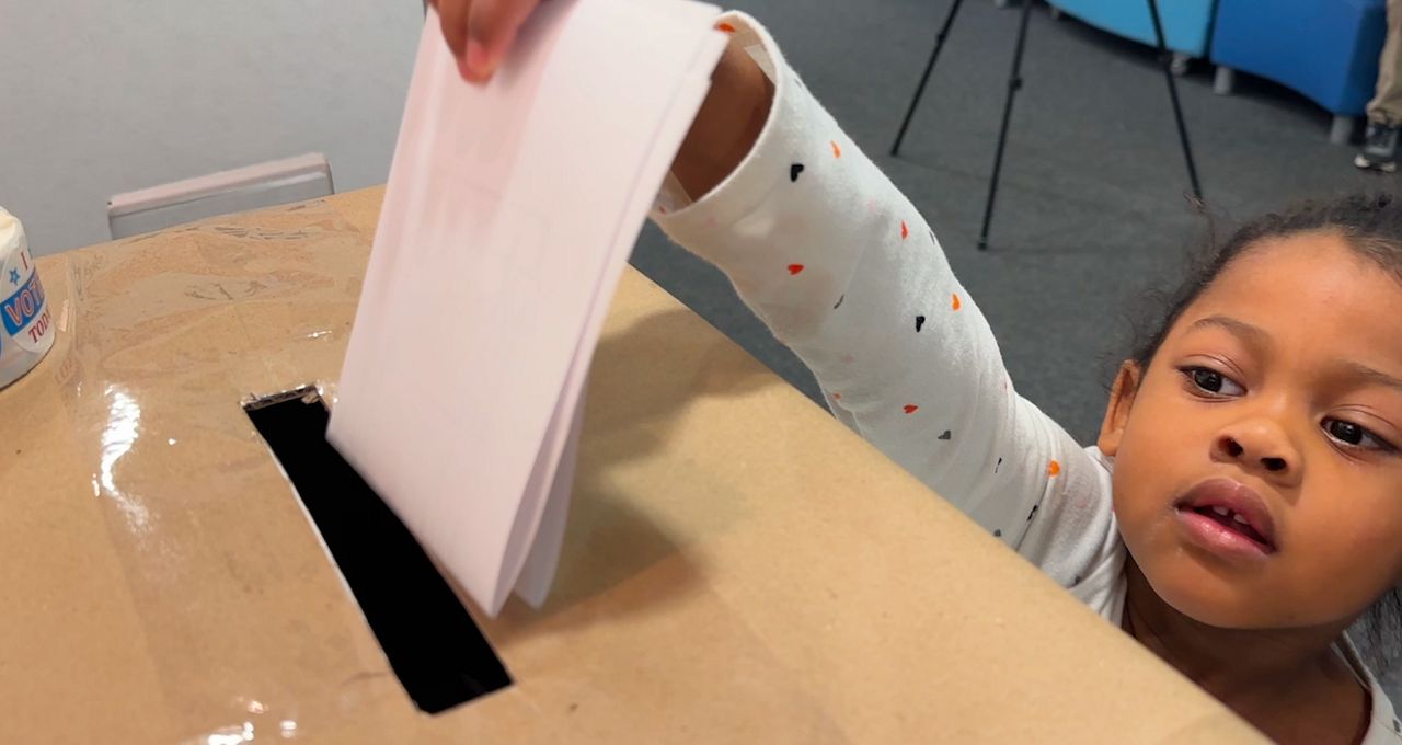 young student voting by slipping a sheet of paper in a cardboard ballot box