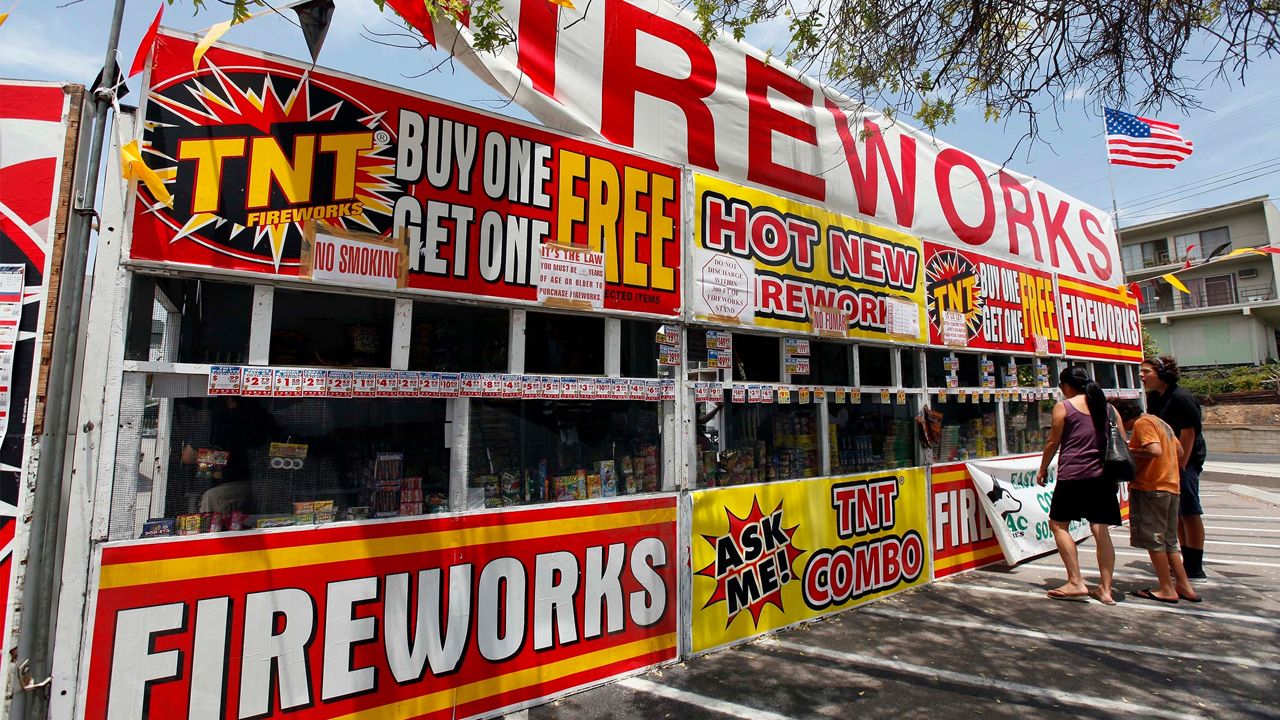 File - In this July 2, 2013, file photo, a family buys fireworks at a TNT Fireworks stand in the City of Monterey Park, Calif. Albuquerque, N.M.; is joining a growing number of communities in California and Texas asking residents to use an app to report illegal fireworks on July 4th instead of calling 911. (AP Photo/Nick Ut, File)