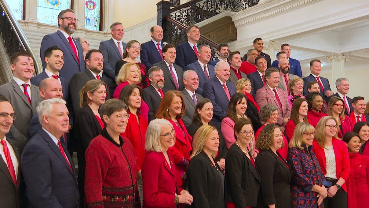Legislators wearing shades of red pose for a photo on a staircase