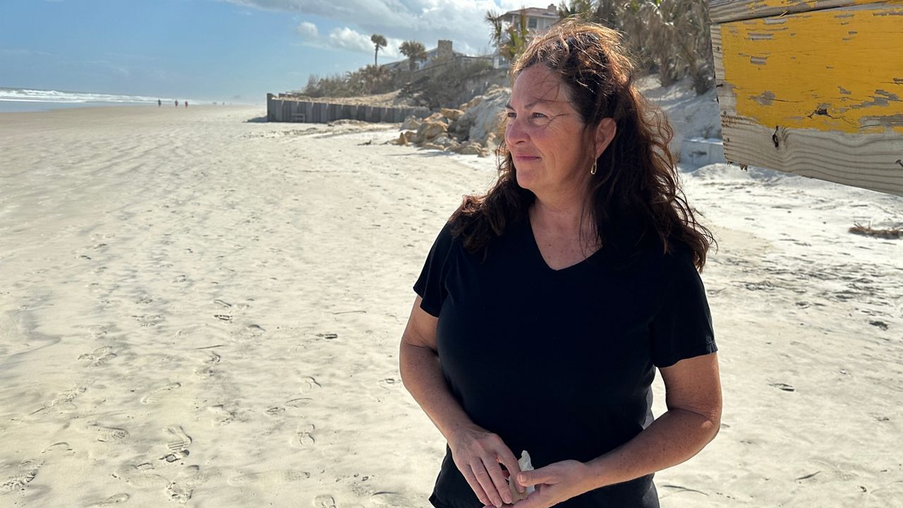 Kelly Walker stands before her Wilbur-by-the-Sea home, which — like her neighbors — faces hundreds of thousands in repairs post hurricanes. (Spectrum News)
