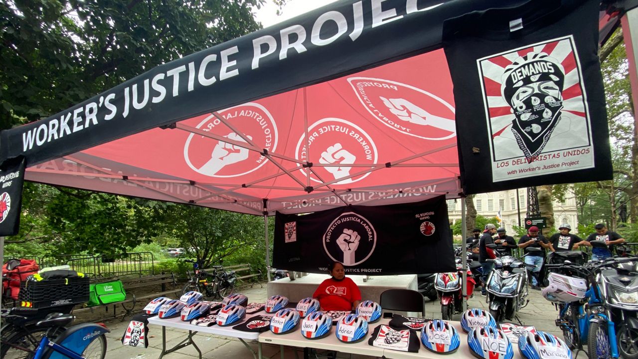 Helmets symbolizing delivery workers who died while on the job adorn the table where Workers Justice Project set up a press conference outside City Hall.