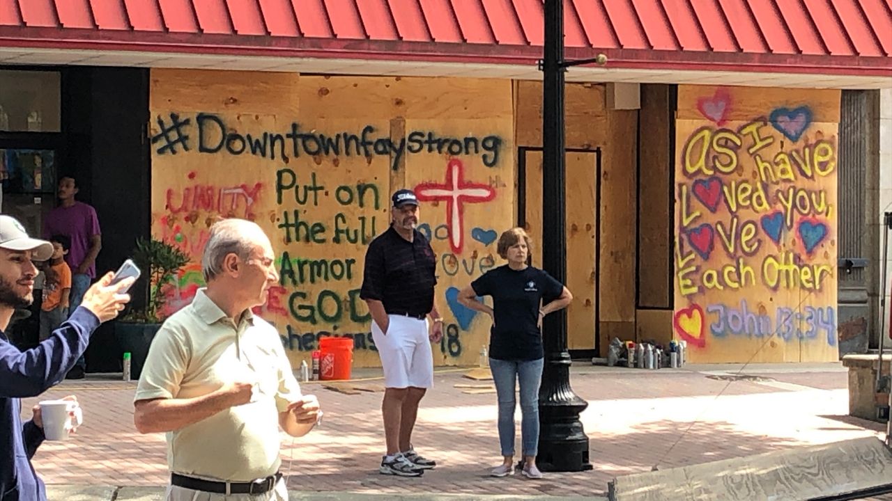 Neighbors stand in front of a boarded-up business in downtown Fayetteville Sunday morning. Officials have declared a curfew beginning at 7 p.m.
