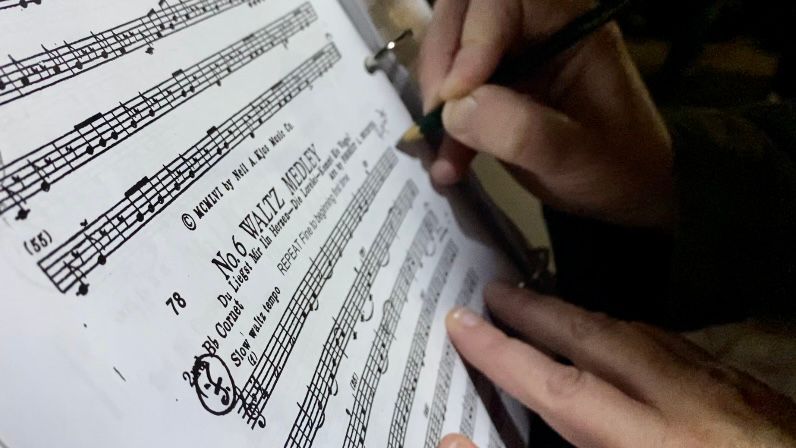 The band director for the Little German Band and Dancers makes a note on a music score. (Spectrum News 1/Rachel Boyd) 