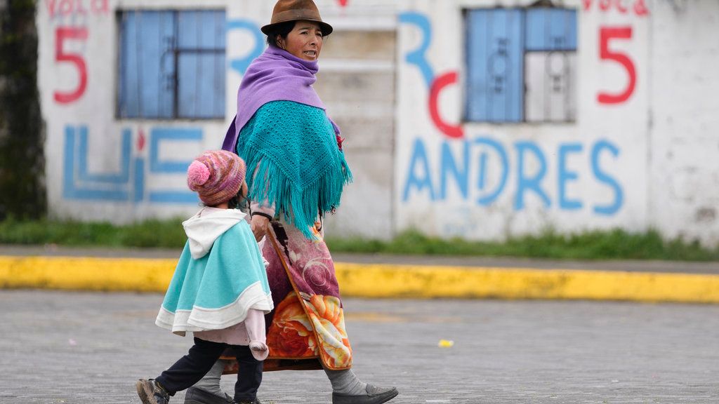 Una mujer indígena y su hija caminan junto a murales de campaña en Cochapamba, Ecuador.