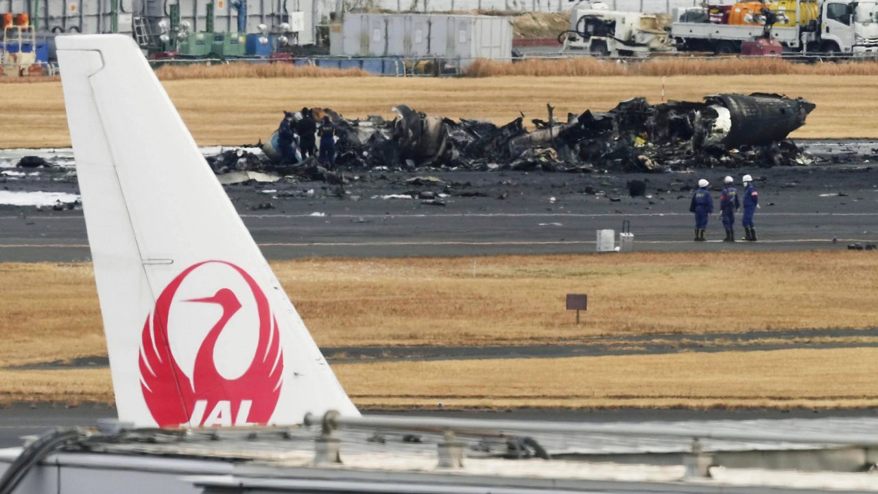 The burn-out Japanese coast guard aircraft is seen at rear behind the logo of Japan Airline at Haneda airport on Wednesday, Jan. 3, 2024, in Tokyo, Japan. (Kyodo News via AP)