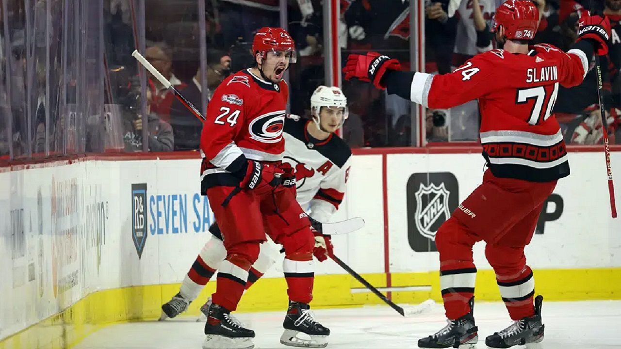 Carolina Hurricanes' Seth Jarvis (24) celebrates his goal with Jaccob Slavin (74) with New Jersey Devils' Jack Hughes (86) during the first period of Game 1 of an NHL hockey Stanley Cup second-round playoff series in Raleigh, N.C., Wednesday, May 3, 2023. (AP Photo/Karl B DeBlaker)