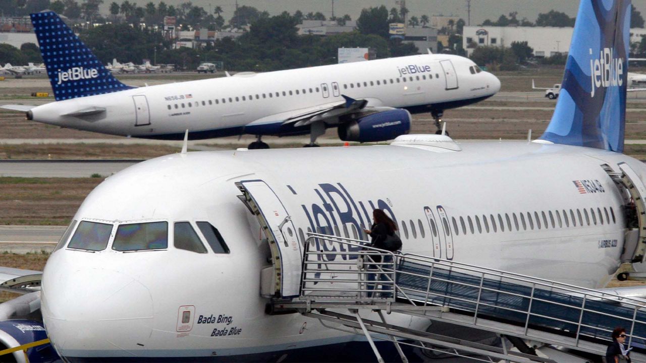 A passenger boards a JetBlue plane as another takes off at rear at Long Beach Airport in Long Beach, Calif., Tuesday, Oct. 25, 2011. The New York-based airline says its 2011 third-quarter net income fell 41 percent as higher fuel costs and bad weather offset higher revenue from fares and fees. (AP Photo/Reed Saxon)