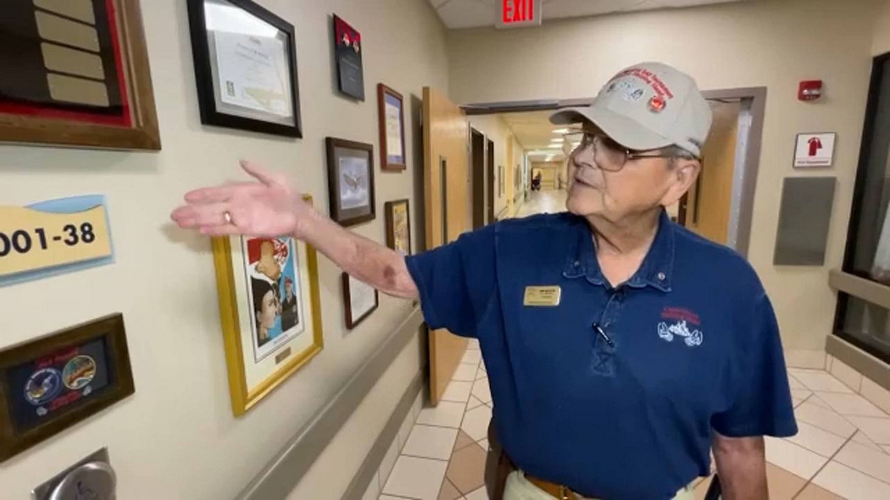 Jim Griffin, chairman of Operation Helping Hand at James A. Haley Veterans' Hospital in Tampa, displays a wall where many pictures, awards and honors given to the organization are displayed. (Spectrum News)