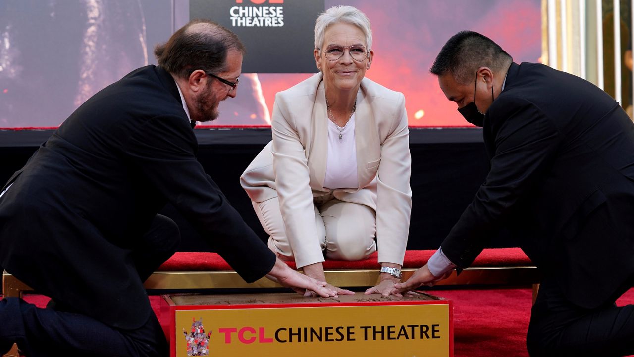 Actor Jamie Lee Curtis, center, gets help pressing her hands in cement during a ceremony for her at the TCL Chinese Theatre, Wednesday, Oct. 12, 2022, in Los Angeles. (AP Photo/Chris Pizzello)