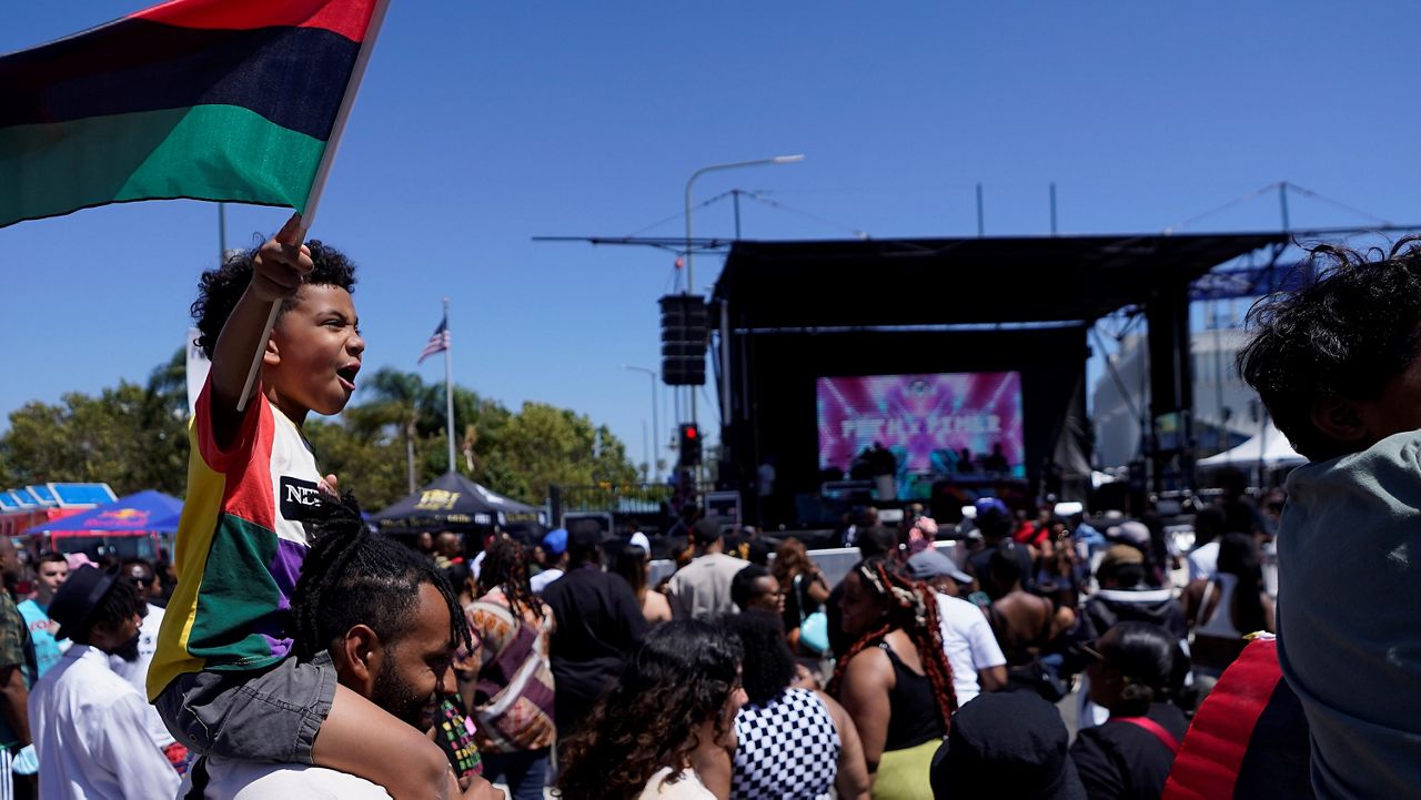 Julien James carries his son, Maison, 4, holding a Pan-African flag, to celebrate during a Juneteenth commemoration at Leimert Park in Los Angeles on June 18, 2022. (AP Photo/Damian Dovarganes)