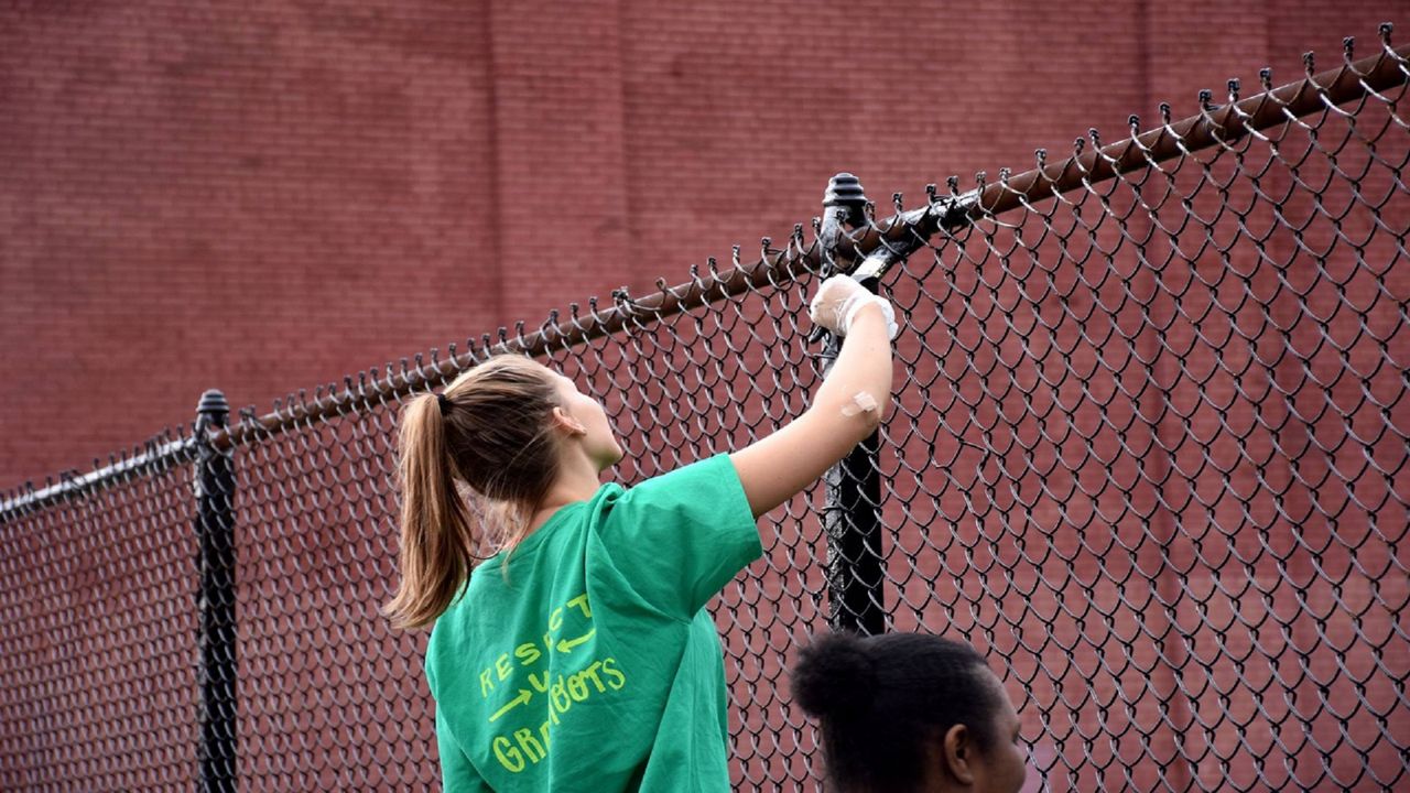 A Keep Cincinnati Beautiful employee paints a fence during a community cleanup event (Casey Weldon | Spectrum News 1)