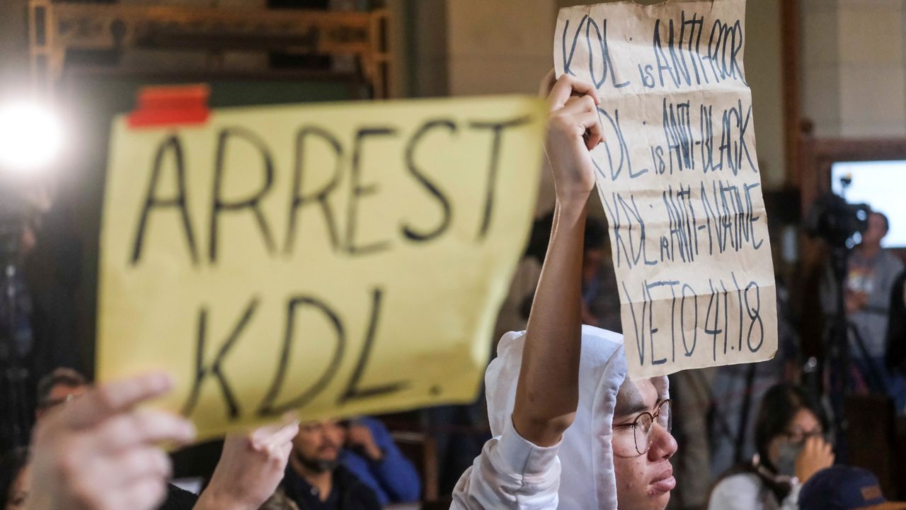 Protesters hold signs and shout slogans during the Los Angeles City Council meeting Tuesday, Dec. 13, 2022 in Los Angeles. A small group of protesters is chanting throughout the meeting calling for the resignations of Councilman Kevin de Leon. (AP Photo/Ringo H.W. Chiu)