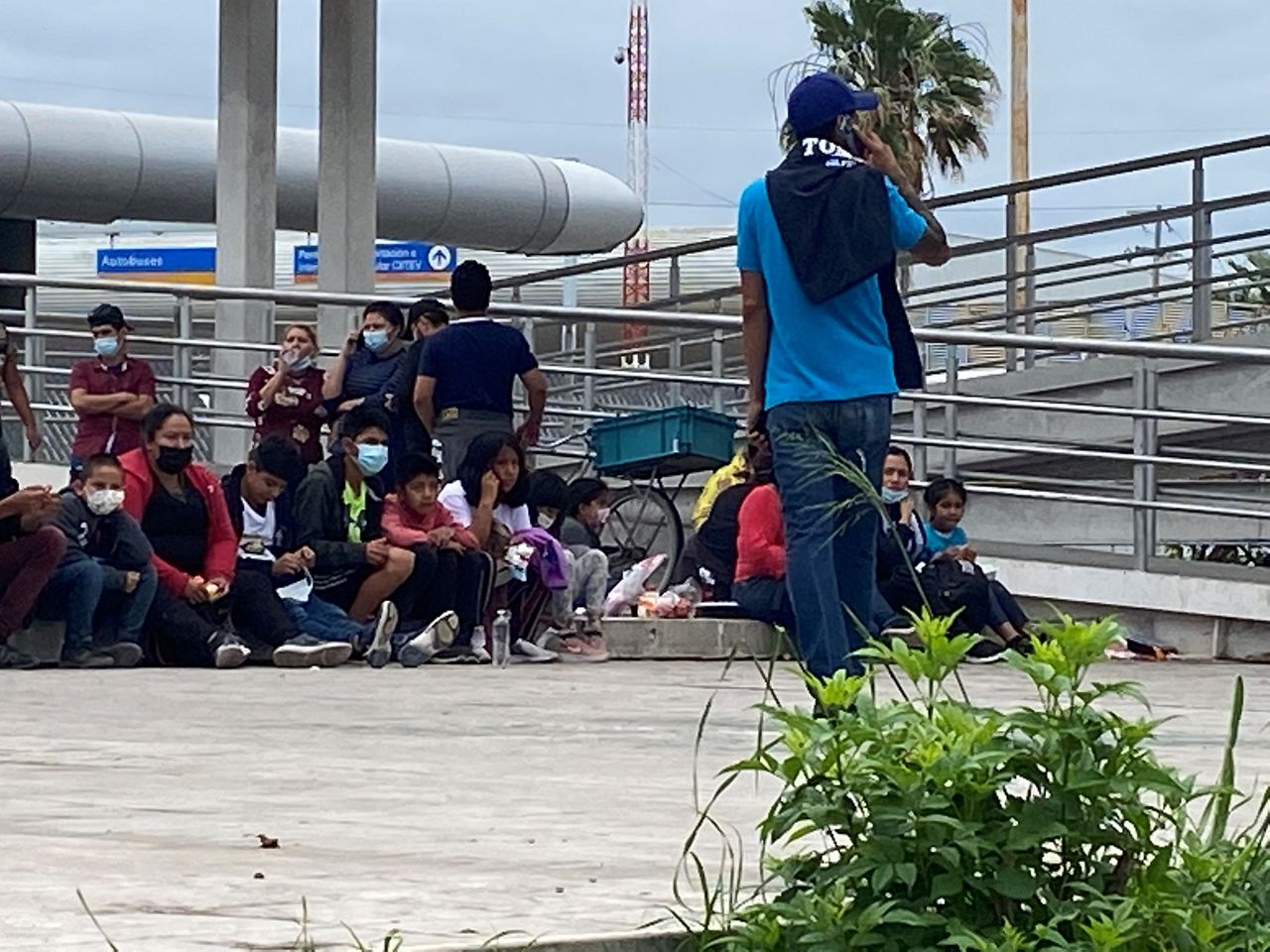 Migrants sit on the stairs of the Mexican customs facility after being expelled to Mexico. (Spectrum News 1/Adolfo Muniz)