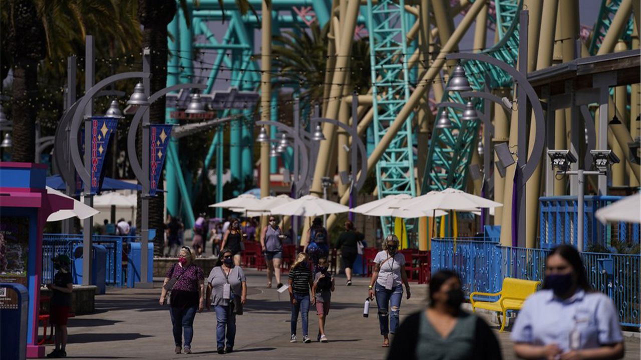 Visitors walk past rides during the Knott's Taste of Boysenberry Festival at Knott's Berry Farm in Buena Park, Calif., Tuesday, March 30, 2021. Massive Los Angeles County can reopen even more businesses, California public health officials announced Tuesday. The county of 10 million people was one of several counties, including neighboring Orange County, that moved into the state's second-least restrictive orange tier amid low coronavirus case rates. (AP Photo/Jae C. Hong)