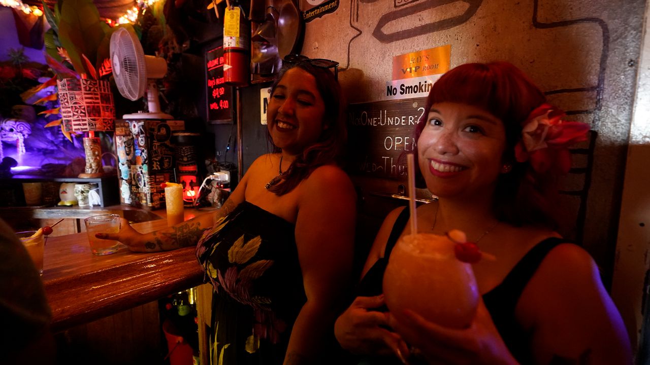 Patrons Verona Leyva, left, and Michelle Perez enjoy cold tropical cocktails in the tiny interior of the Tiki-Ti bar as it reopens on Sunset Boulevard in Los Angeles, Wednesday, July 7, 2021. (AP Photo/Damian Dovarganes)