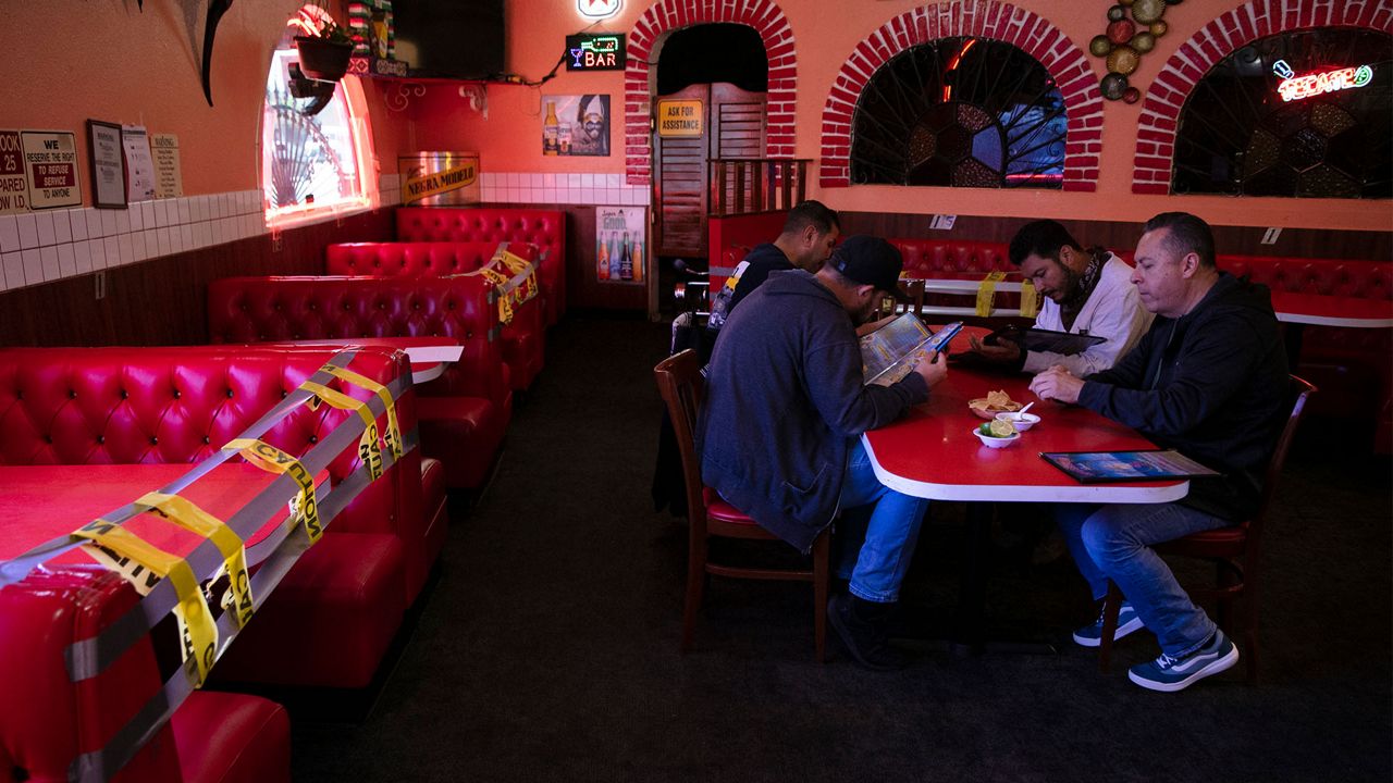 Dine-in customers look at menus as dining booths are taped off for social distancing at Mariscos Linda restaurant, Wednesday, July 1, 2020, in Los Angeles. California Gov. Gavin Newsom has ordered a three-week closure of bars and indoor operations of restaurants certain other businesses in Los Angeles and 18 other counties. (AP Photo/Jae C. Hong)