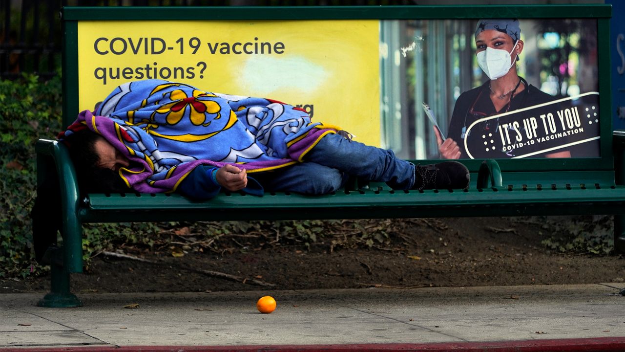 A homeless person sleeps on a bench in downtown Los Angeles, Wednesday, Dec. 15, 2021. (AP Photo/Damian Dovarganes)