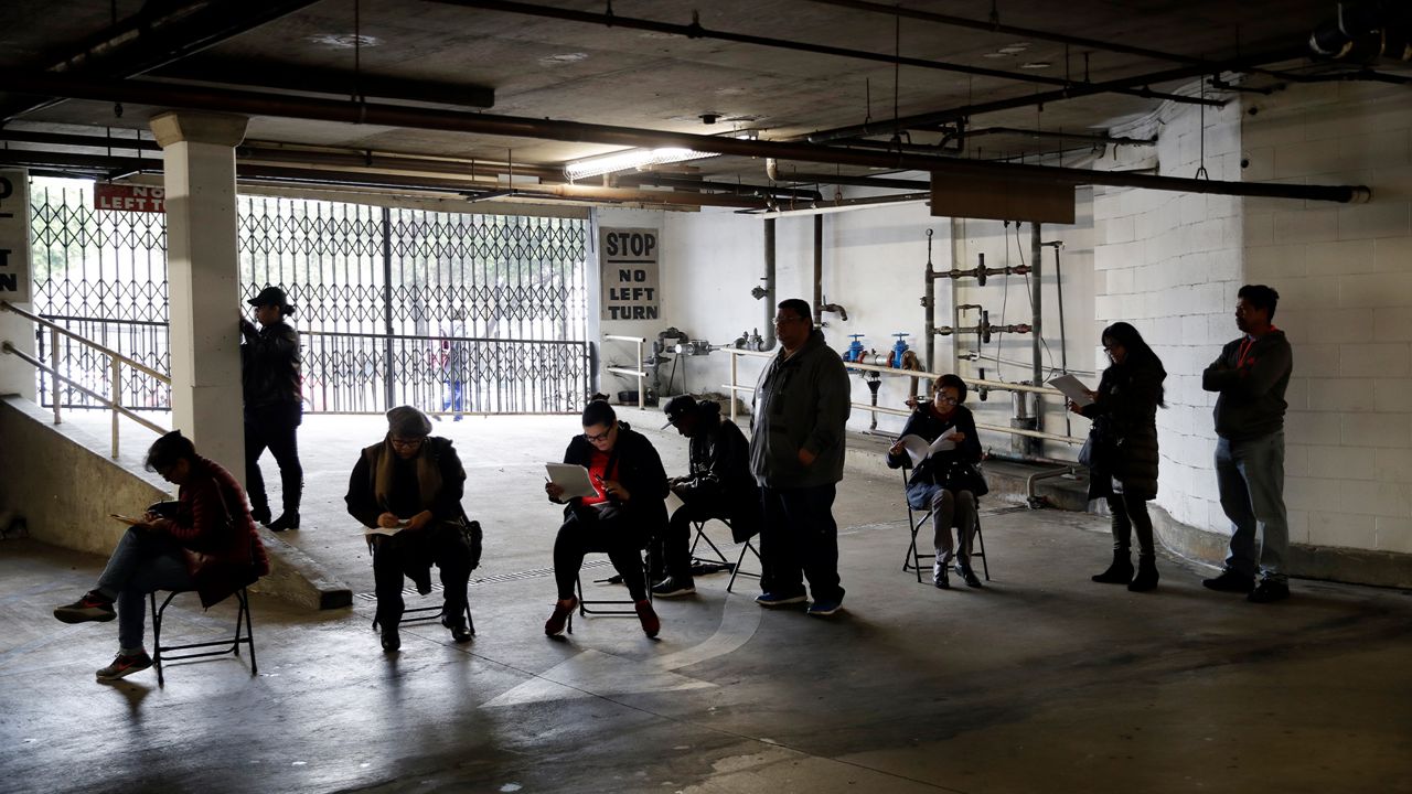 In this March 13, 2020, file photo, unionized hospitality workers wait in line in a basement garage to apply for unemployment benefits at the Hospitality Training Academy in Los Angeles. (AP Photo/Marcio Jose Sanchez, File)