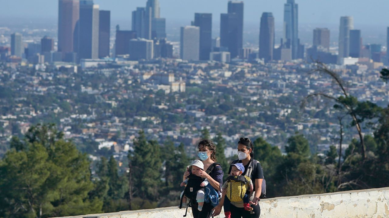 Visitors carry toddlers while walking past of the view of the downtown skyline amid the COVID-19 pandemic on Griffith Park Tuesday, March 9, 2021, in Los Angeles. (AP Photo/Marcio Jose Sanchez)