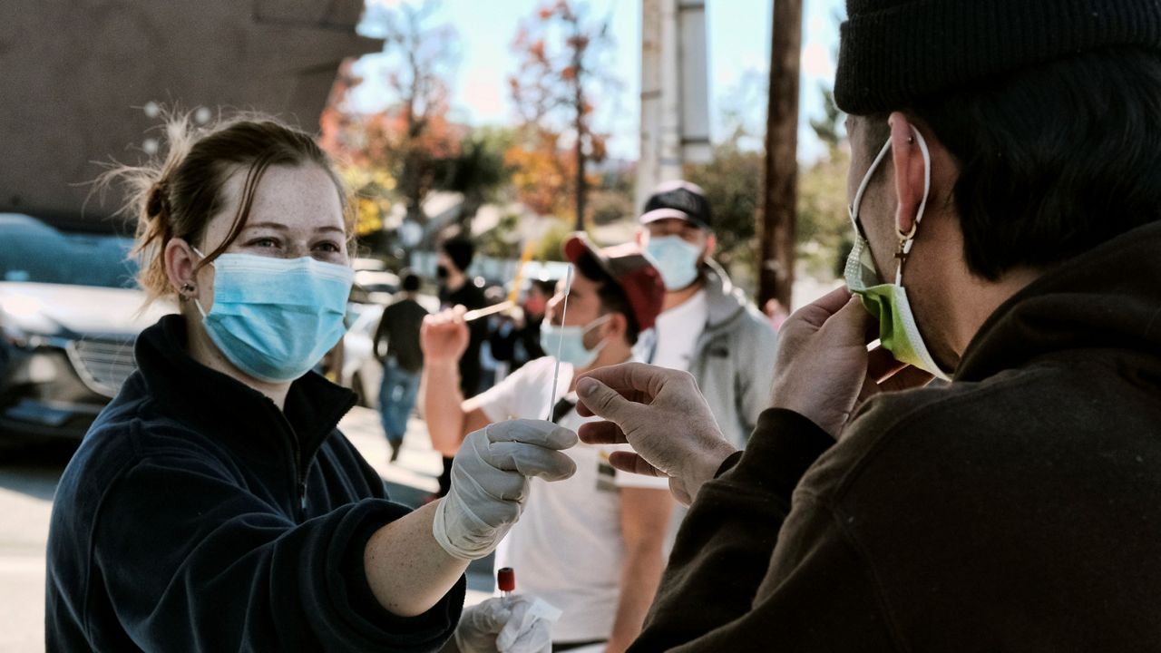 A man is handed a swab for a COVID-19 rapid test as people line up at a gas station in the Reseda section of Los Angeles on Dec. 26, 2021. (AP Photo/Richard Vogel)