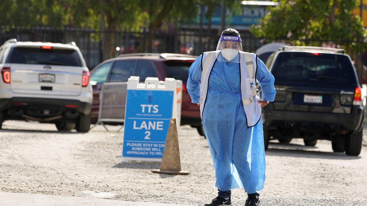 A worker stands in front of a line of vehicles at a COVID-19 testing site Wednesday, Jan. 26, 2022, in the Boyle Heights section of Los Angeles. (AP Photo/Marcio Jose Sanchez)