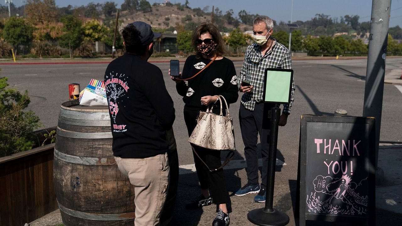Marta McKay, center, and her husband, Bob, show a restaurant worker their proof of COVID-19 vaccination as they enter Highland Park Brewery Monday, Nov. 8, 2021, in Los Angeles. (AP Photo/Jae C. Hong)