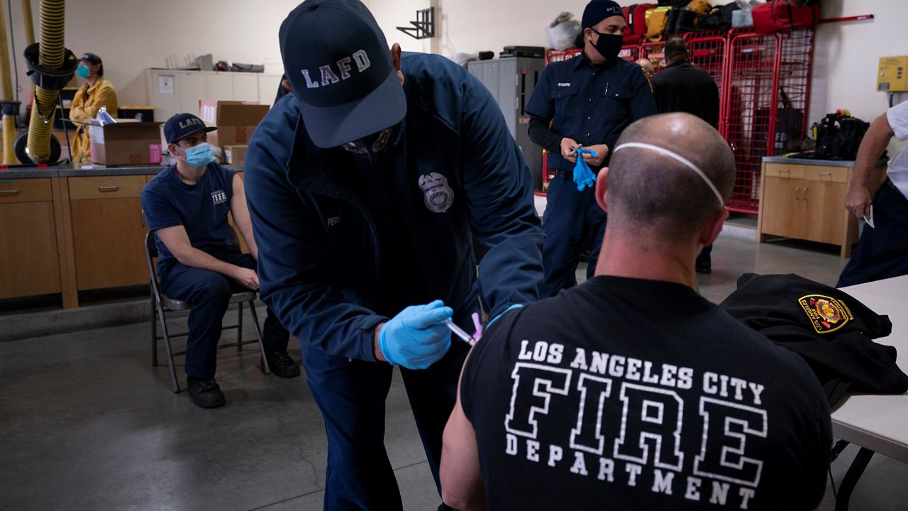 In this Jan. 27, 2021, file photo, firefighter Adam Brandos, right, receives his second dose of the COVID-19 vaccine from Michael Perez at a fire station in Los Angeles. (AP Photo/Jae C. Hong, File)