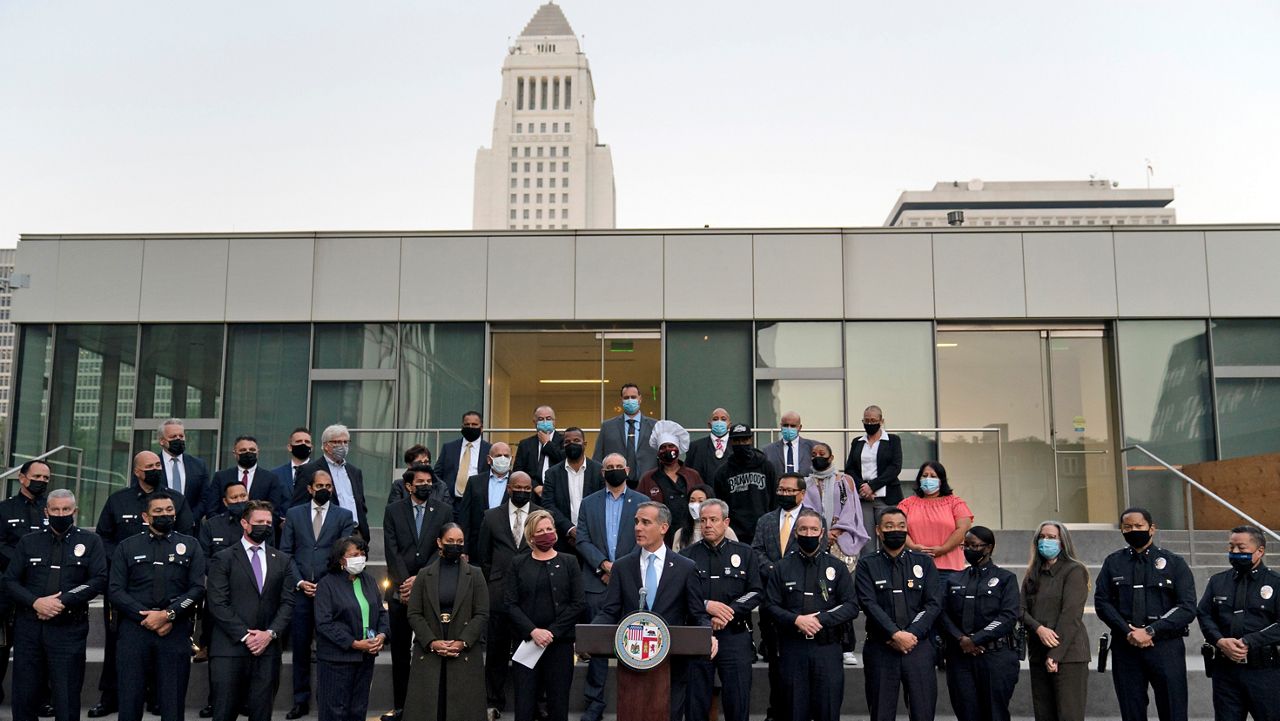 Joined by business owners and community leaders, Los Angeles Mayor Eric Garcetti, center, speaks during a news conference outside the Los Angeles Police Headquarters as City Hall is visible in the background in Los Angeles Thursday, Dec. 2, 2021. (AP Photo/Jae C. Hong)