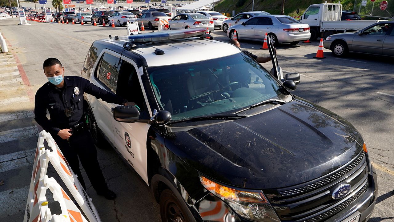 Los Angeles Police officers guard the main entrance to the vaccination center at Dodger Stadium as thousands of motorists wait in line for their vaccine without disruptions in Los Angeles Saturday, Feb. 27, 2021. (AP Photo/Damian Dovarganes)