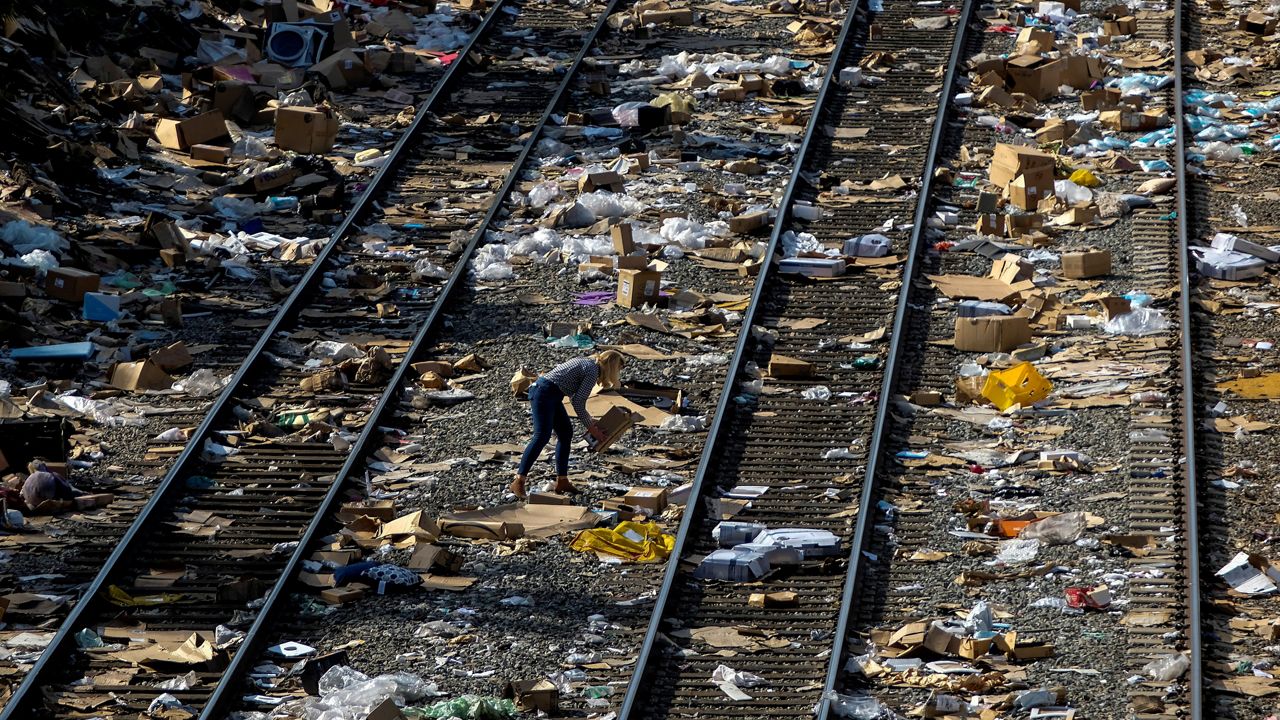 A member of the media picks up a shredded box at a section of the Union Pacific train tracks in downtown Los Angeles, Friday, Jan. 14, 2022. (AP Photo/Ringo H.W. Chiu)