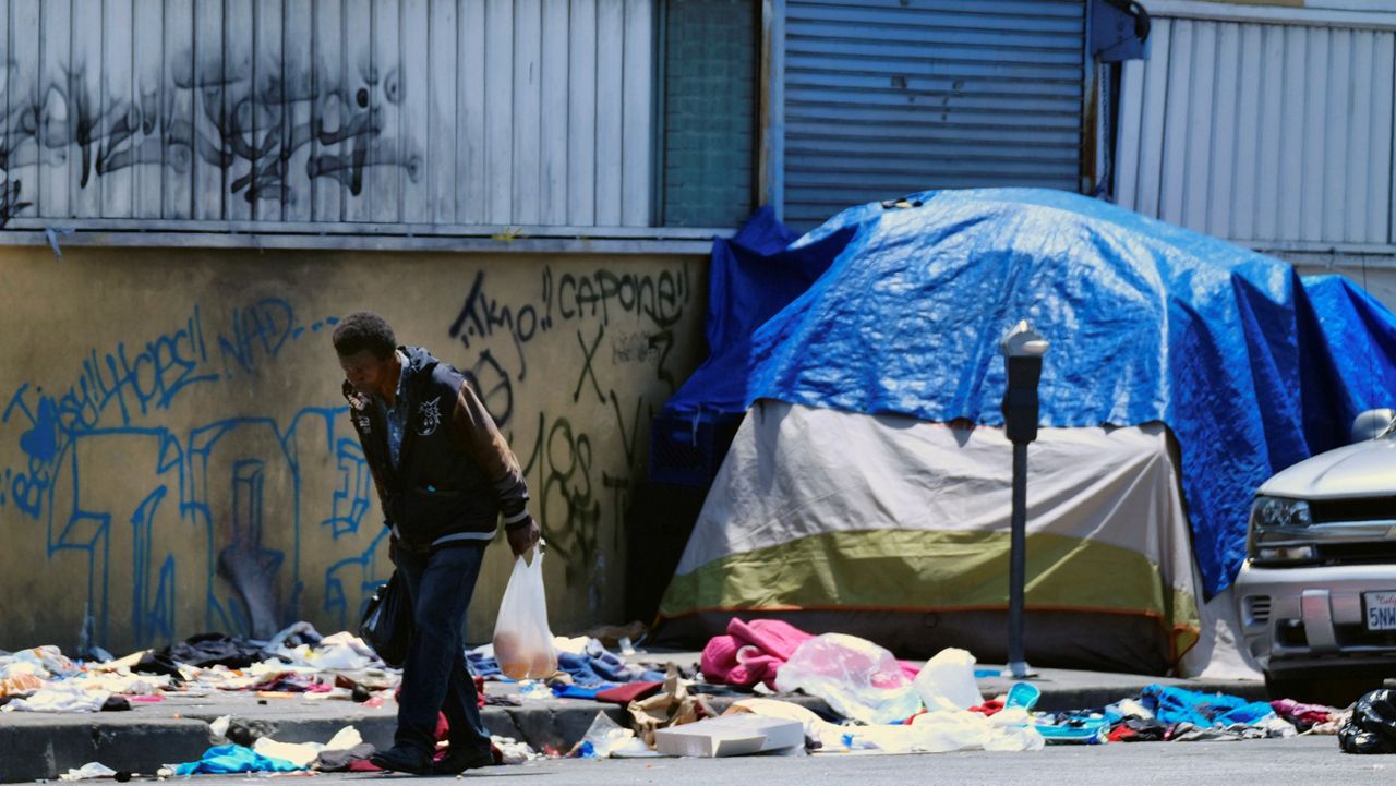 In this May 30, 2019, file photo, a homeless man walks along a street lined with trash in downtown Los Angeles. (AP Photo/Richard Vogel)