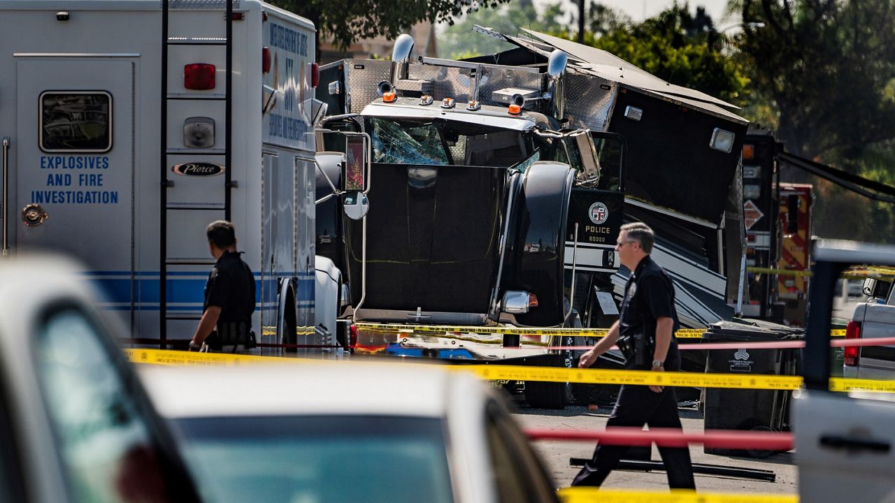 Police officers walk past the remains of an armored Los Angeles Police Department tractor-trailer July 1, 2021, after illegal fireworks seized at a home exploded in South Los Angeles. (AP Photo/Damian Dovarganes, File)