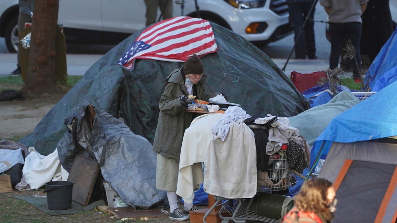 A woman eats at her tent at the Echo Park homeless encampment at Echo Park Lake in Los Angeles, on March 24, 2021. (AP Photo/Damian Dovarganes, File)