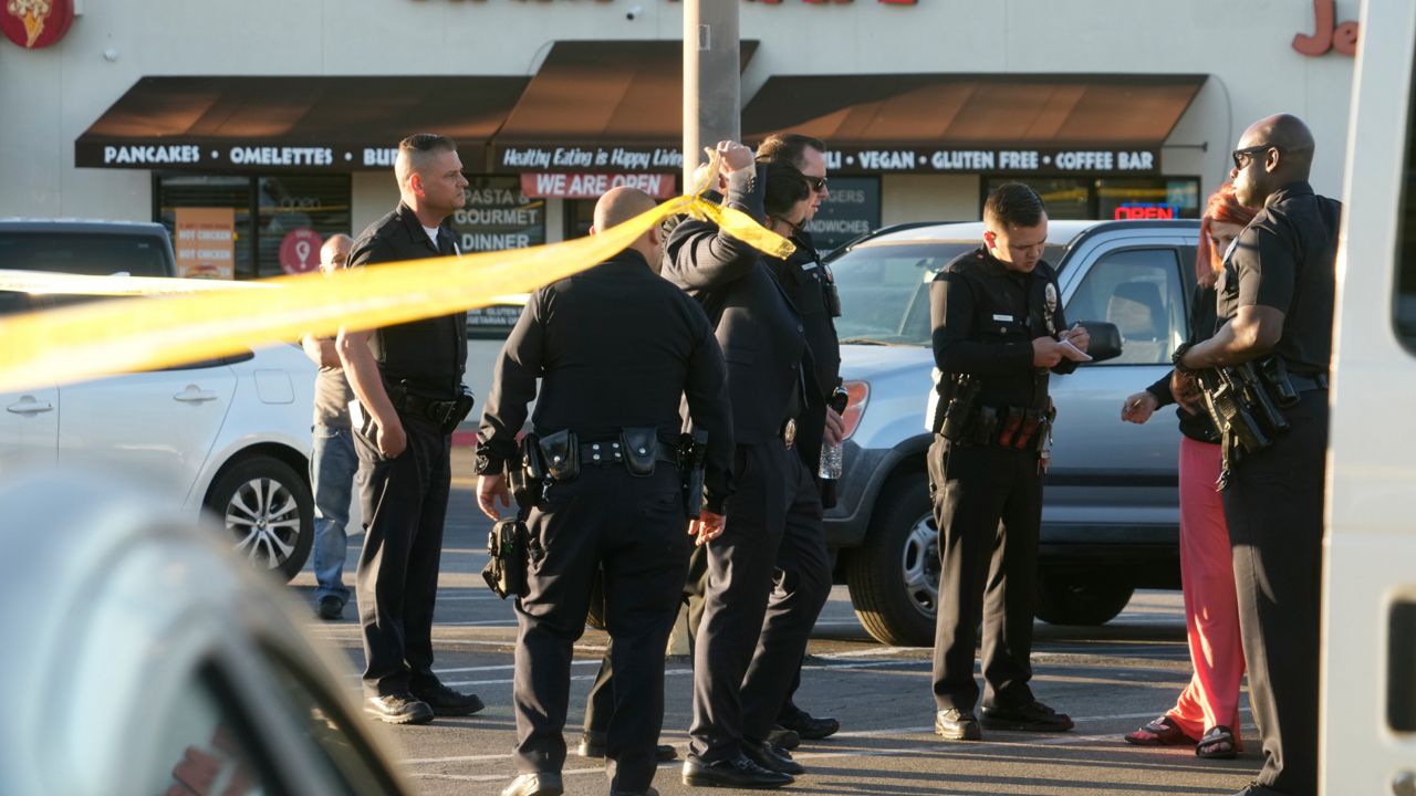 Los Angeles police officers check drivers' licenses before letting shoppers leave the taped-off area of a shopping mall parking lot where a fatal shooting took place, in Los Angeles, Saturday, April 1, 2023. (AP Photo/Damian Dovarganes)