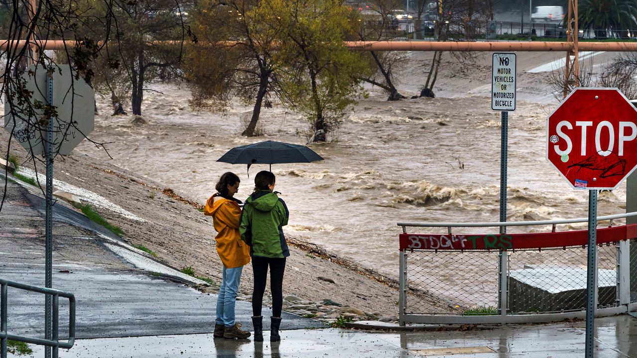 People watch the high volume of storm rain water flowing downstream at the Los Angeles River in Los Angeles on Saturday, Jan. 14, 2023. (AP Photo/Damian Dovarganes)