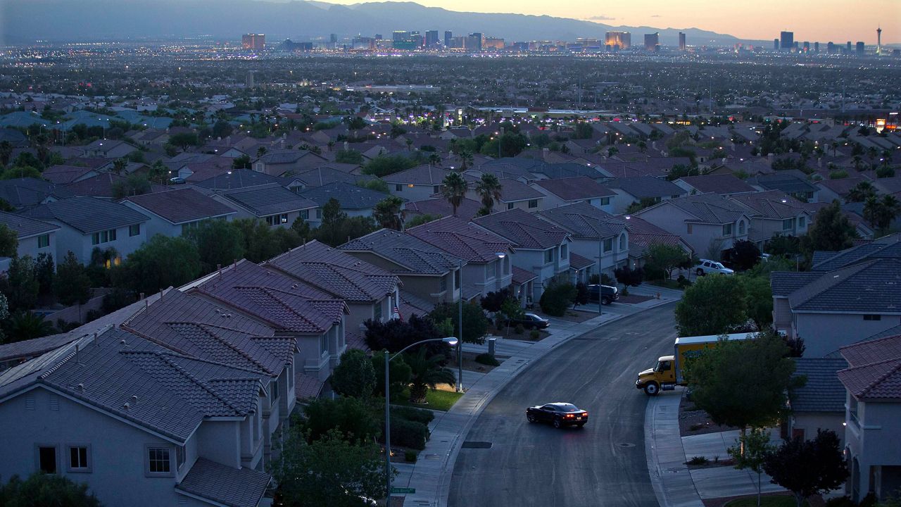 The Las Vegas skyline glows at dusk as a motorist pulls into the driveway of a home, in Henderson, Nev. (AP Photo/Julie Jacobson)