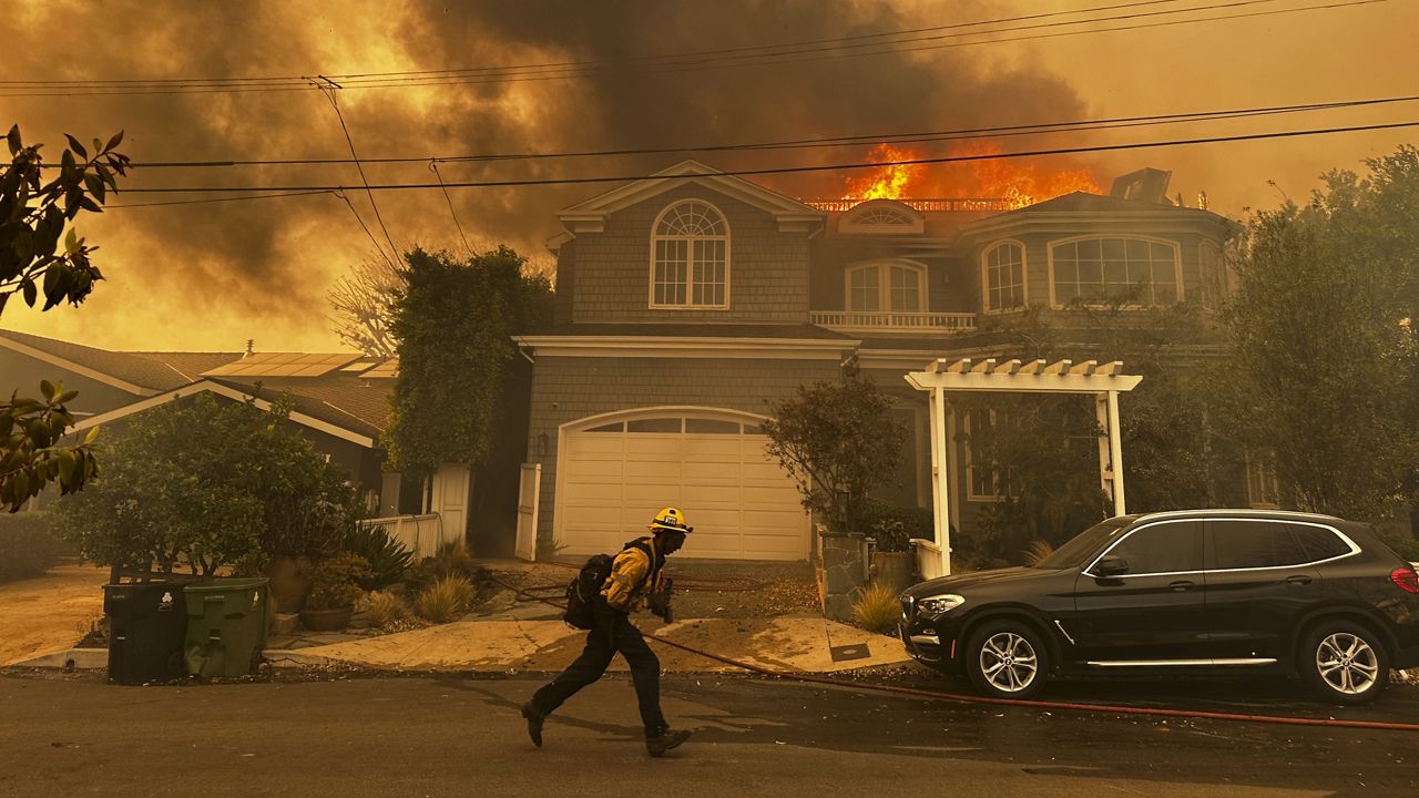 A residence burns as a firefighter battles the Palisades Fire in the Pacific Palisades neighborhood of Los Angeles Tuesday, Jan. 7, 2025. (AP Photo/Eugene Garcia)